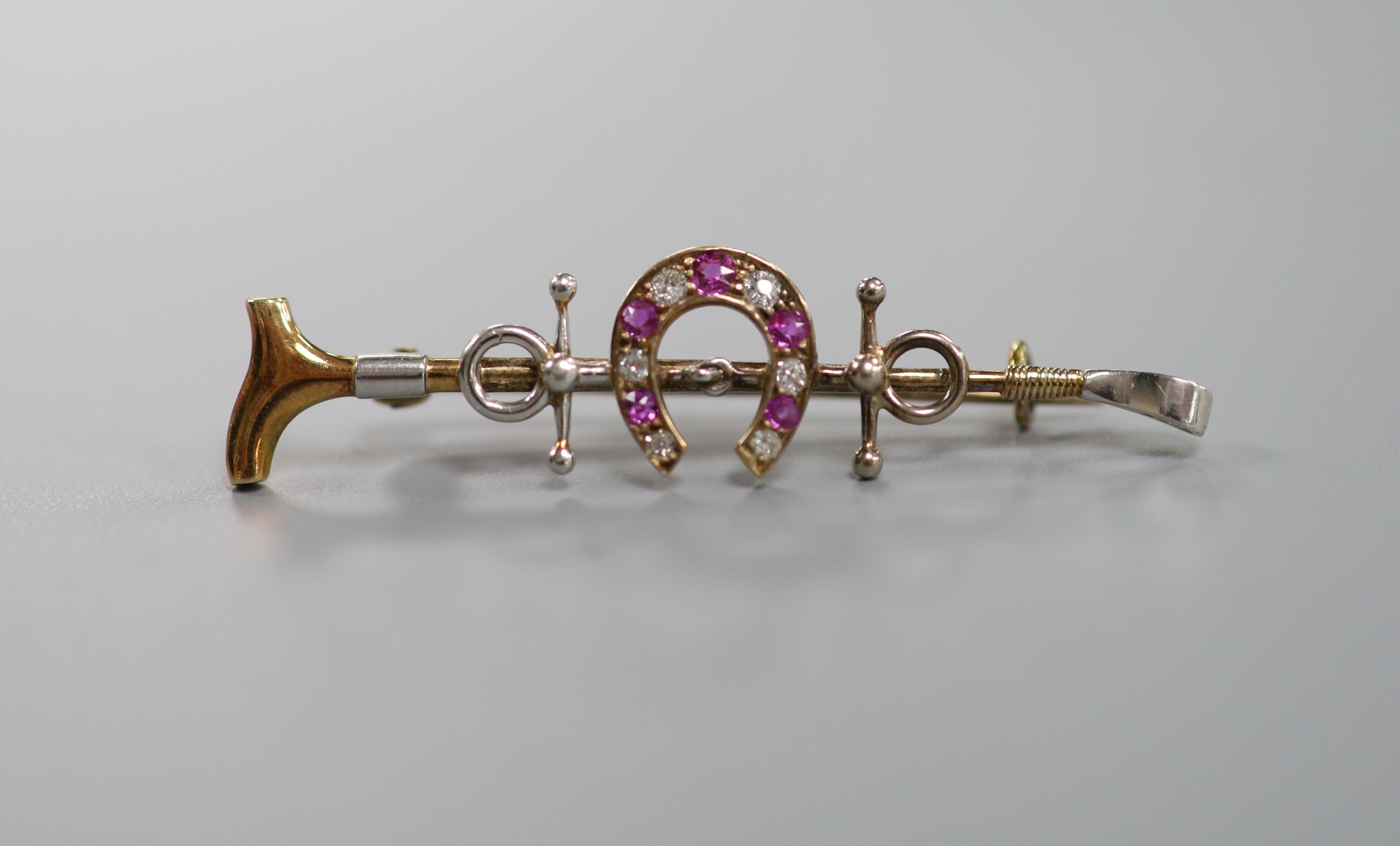A late Victorian yellow metal, ruby and diamond set horseshoe and riding crop bar brooch, 50mm, gross weight 5.4 grams.